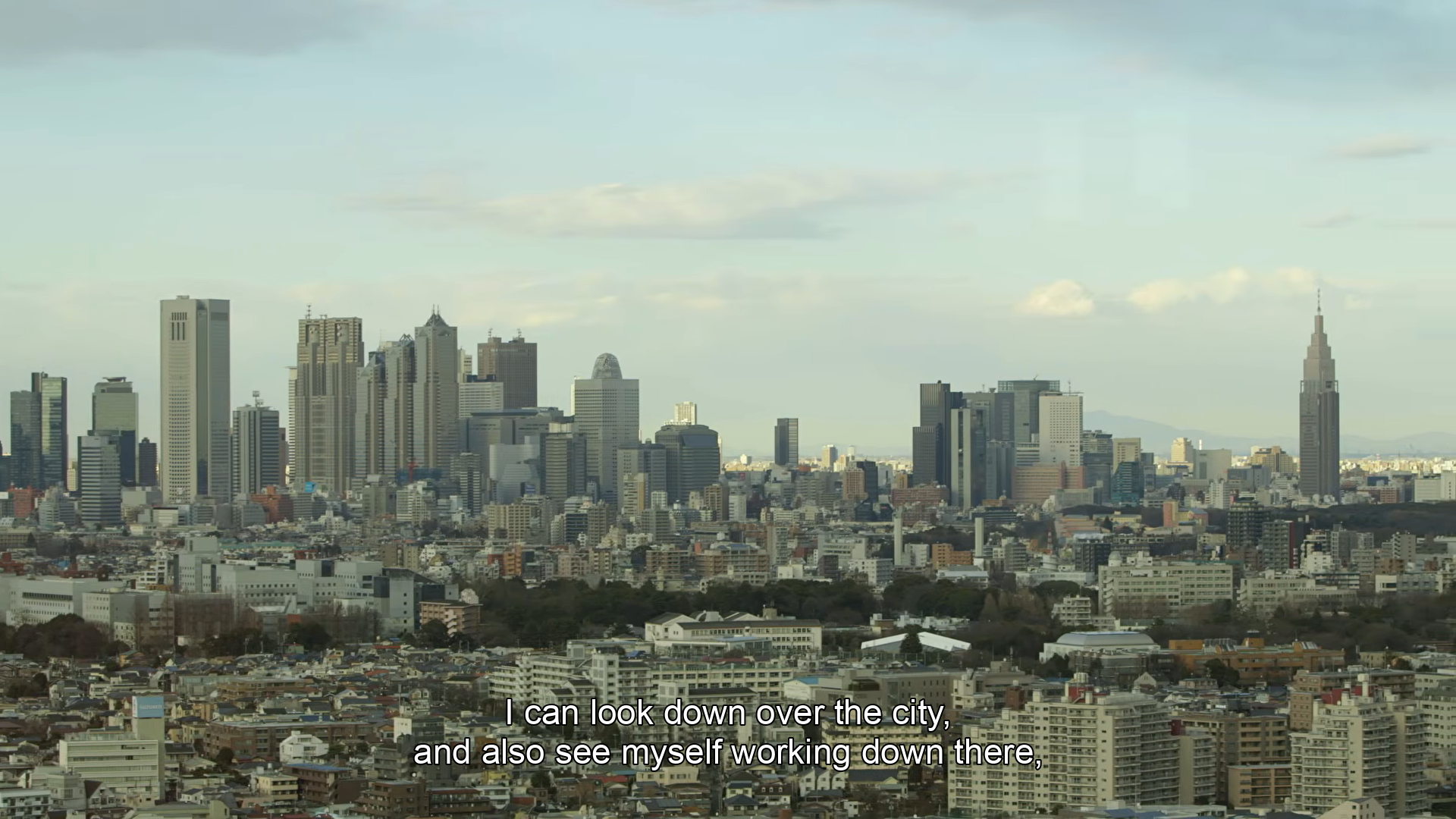 Tokyo skyline from the Hashino interview. English subtitle: “I can look down over the city, and also see myself working down there,”